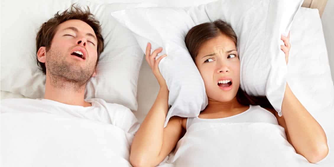 woman covering her ears with pillows with an annoyed expression as partner snores